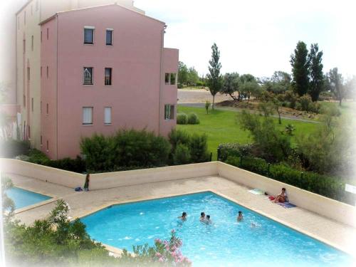 un groupe de personnes dans une piscine à côté d'un bâtiment rose dans l'établissement Résidence Amourêva,T2, vue LAGON, proche mer, parking, clim, piscine, au Cap d'Agde