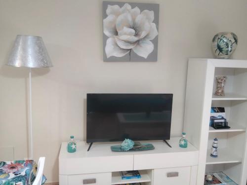 a tv on a white cabinet with a flower on the wall at Apartamento céntrico cerca de la playa in Águilas