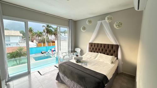 a bedroom with a bed and a balcony with a pool at Hotel Encanto Sol e Mar in Caraguatatuba