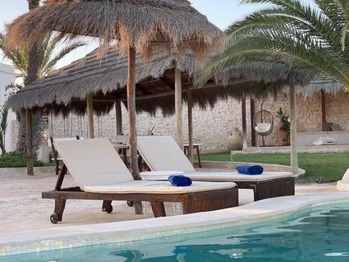 a pool with two lounge chairs and a thatch umbrella at Menzel Al karam, in Temlale