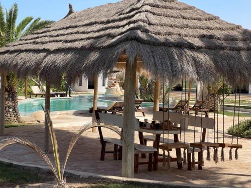a table and chairs under a straw umbrella next to a pool at Menzel Al karam, in Temlale