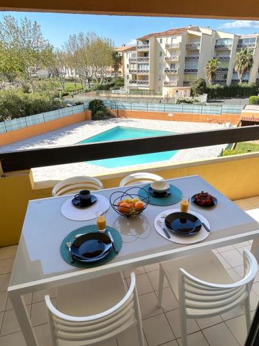 - une table avec des assiettes de nourriture sur un balcon avec une piscine dans l'établissement CAP AU CAP - T3 avec Clim WIFI Vue piscine proximité plage Richelieu, au Cap d'Agde