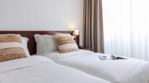 two beds in a hotel room with white sheets and pillows at Albergaria Quim Barreiros in Vila Praia de Âncora