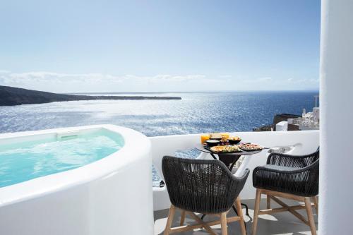a balcony with a table and chairs next to a swimming pool at ArmonOia Luxury Caves in Oia