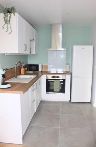 une cuisine avec des armoires blanches et un réfrigérateur blanc dans l'établissement Apptartement neuf - Situation idéale - Balnéo - Parking, à Mérignac