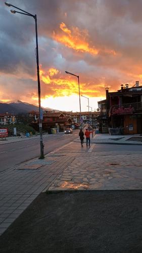 2 personnes marchant dans une rue au coucher du soleil dans l'établissement Hotel Casa karına bansko, à Bansko