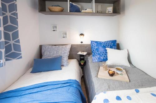 two beds in a small room with blue and white pillows at Bungalow Bord de mer in Gouville-sur-Mer