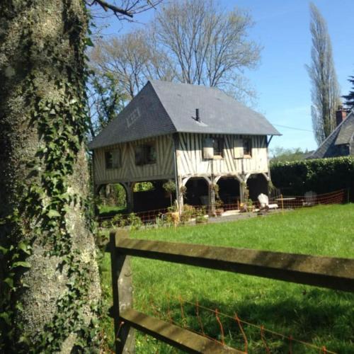 una grande casa in legno in un campo con un albero di La CHARETTERIE Gites du Manoir de La Porte a Les Authieux-sur-Calonne