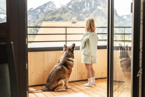 a woman looking out a window at a dog sitting on a balcony at Alpen Krone Kehlegg in Dornbirn