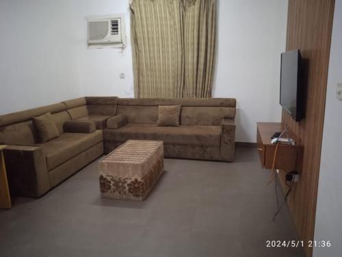 een woonkamer met een bruine bank en een tv bij Wajood Services Apartment بناية وجود للشقق الفندقية in Salalah