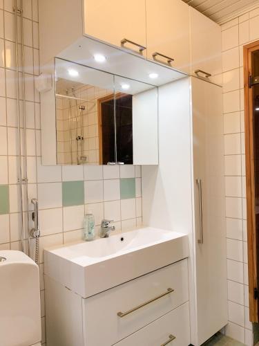 La salle de bains blanche est pourvue d'un lavabo et d'un miroir. dans l'établissement Rovaniemi City Centre Apartment, private sauna, à Rovaniemi
