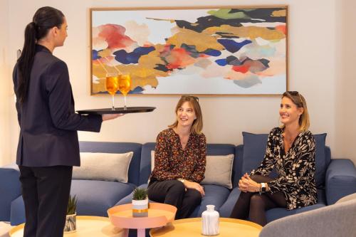 a woman is presenting a tray of drinks to two women at Staybridge Suites - Cannes Centre by IHG in Cannes