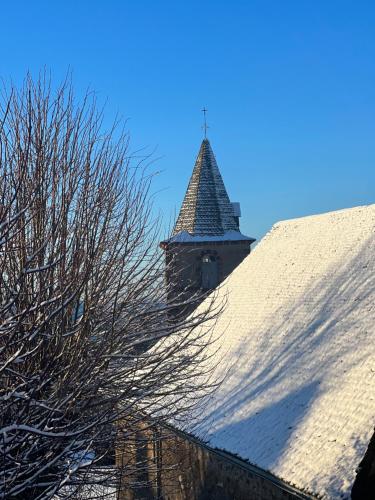 a snow covered roof with a tower in the background at Maison d'Hôtes & Savonnerie de Bonnefon in Saint-Chély-dʼAubrac