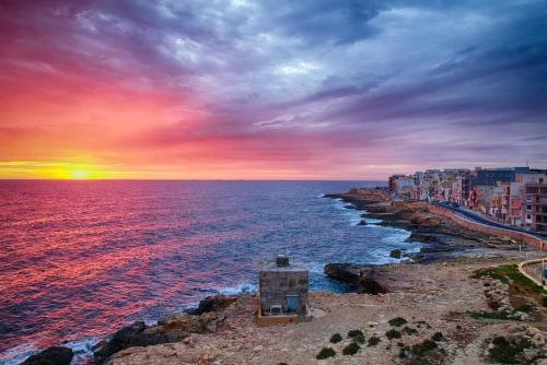 een zonsondergang over de oceaan met een gebouw aan de kust bij Star Dream Apartment in Xgħajra