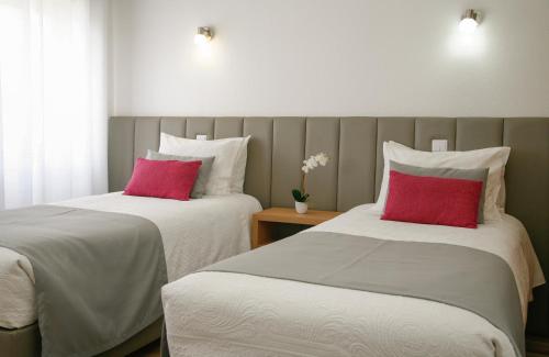 two beds with white and red pillows in a room at Nova Delpa AL in Caldas da Rainha