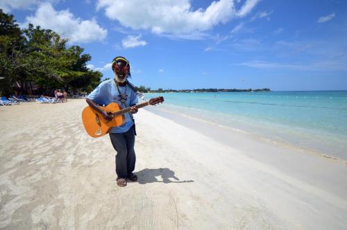 a man standing on a beach holding a guitar at Sunset at the Palms Resort - Adults Only - All Inclusive in Negril
