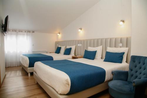 a hotel room with two beds and a chair at Nova Delpa AL in Caldas da Rainha