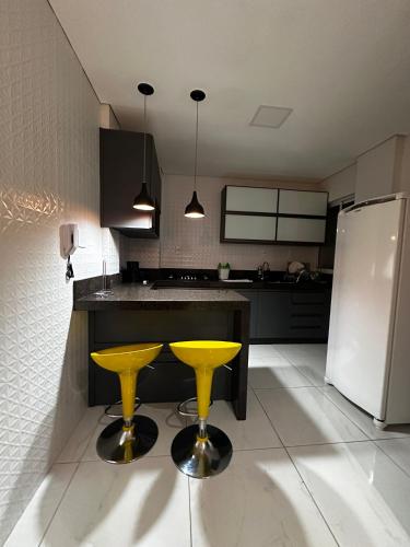 een keuken met 2 gele barkrukken en een koelkast bij Apartamento em área nobre in Conselheiro Lafaiete