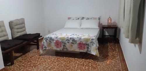a bedroom with a bed with a flowered blanket and a chair at Ponta Negra Hospedagem in Maricá