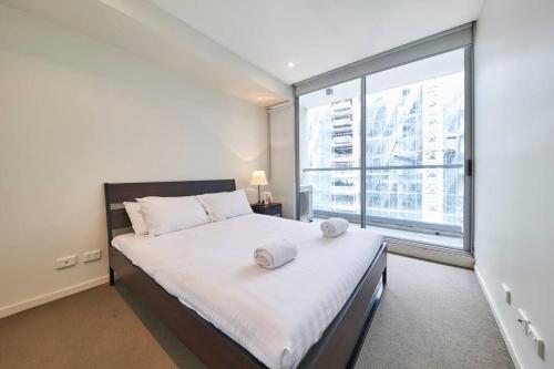 a bedroom with a large white bed with a large window at Docklands Convenient & Modern 1 Bed Apartment in Melbourne