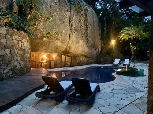 a swimming pool with chairs and a rock wall at Casa da Pedra Atibaia Clube da Montanha in Atibaia