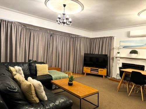 a living room with a black leather couch and a television at Tauranga - Stylish & Centrally Located Near Hospital in Tauranga