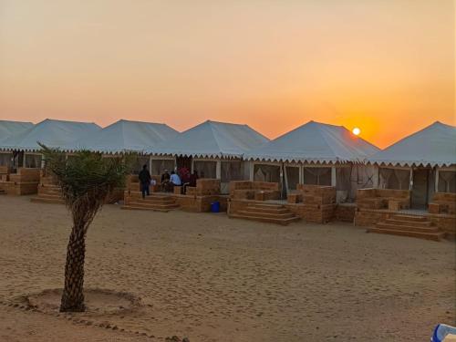 a group of tents on a beach with a palm tree at THE THAR DESERT CAMP SAM JAISLMER in Sām