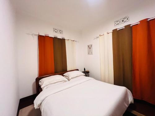 um quarto com uma cama com lençóis brancos e cortinas laranja em Makini Spaces em Arusha