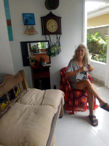 uma mulher sentada numa cadeira numa sala com um relógio em Xixova Hostel Japui são Vicente na Praia Grande