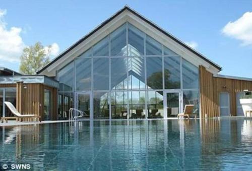 un gran edificio de cristal con una piscina frente a él en Roseberry Cottage - Lower Mill Estate, en Somerford Keynes