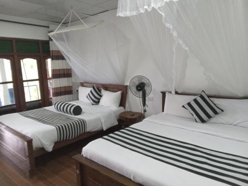 two beds in a room with white walls and windows at Chamodya Home Stay in Ella