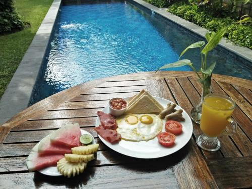 een bord met ontbijtproducten op een tafel naast een zwembad bij Sekuta Condo Suites in Sanur