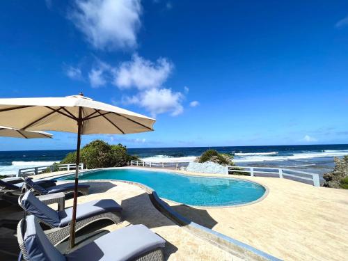 a swimming pool with chairs and an umbrella and the ocean at Balay Pacifico in Sarog