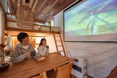 two people sitting at a table in a room with a tv at サウナ・ジャグジー・完全貸し切りという贅沢　大人の秘密基地　Tiny Cabin TATEGU#02 in Miyota