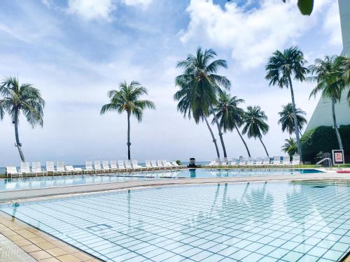 a swimming pool with palm trees and chairs at Regency Tanjung Tuan Beach PD by Idealhub in Port Dickson