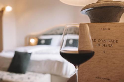 ein Glas Wein neben einem Bett in der Unterkunft Wine Resort Campacci in San Gusmè