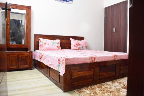 a bedroom with a wooden bed with pink sheets at Budget Friendly 3 BHK + Prime Location in Faridabad