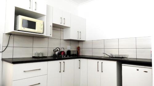 Biała kuchnia z białymi szafkami i kuchenką mikrofalową w obiekcie Die Regte Plek w mieście Despatch