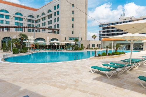 una piscina en un hotel con sillas y sombrillas en Millennium Palestine Ramallah en Ramallah