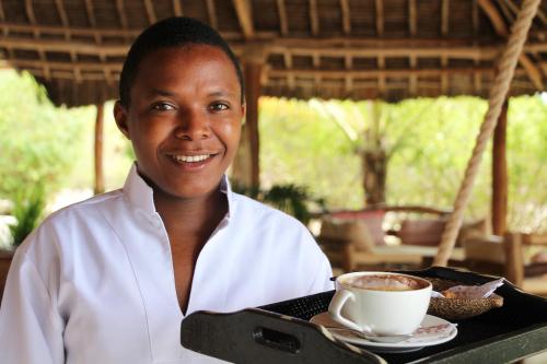a woman holding a tray with a cup of coffee at The Charming Lonno Lodge Watamu in Watamu