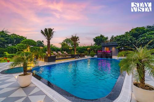 una piscina en un complejo con palmeras en StayVista's Hampton Acres - Outdoor Pool, Vast Lawn & Terrace, en Dhauj