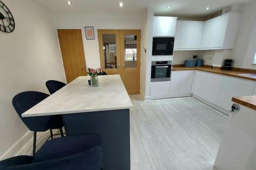 une cuisine avec des placards blancs et un comptoir avec des chaises bleues dans l'établissement Village Home -Syston, Leicestershire, à Syston
