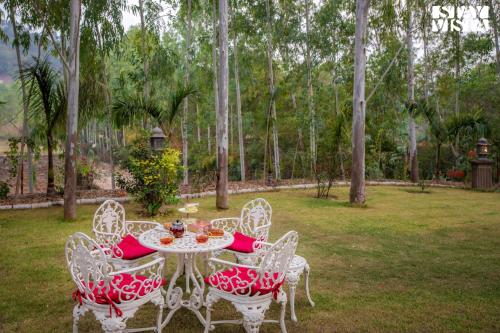 una mesa con sillas rojas y blancas en un patio en StayVista's Silver Slopes - Mountain-View Villa with Outdoor Pool, Expansive Lawn featuring a Gazebo & Terrace, en Chandīgarh