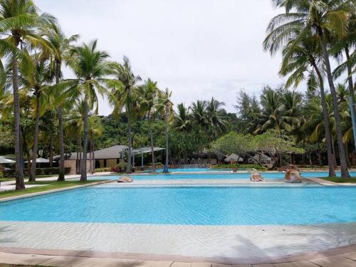 a swimming pool with palm trees and people in it at 2BR Penthouse in Anvaya Cove in Morong