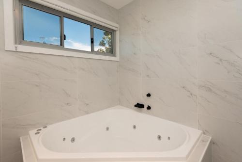 a white bathroom with a tub and a window at BEACHFRONT BLISS / BROULEE in Broulee
