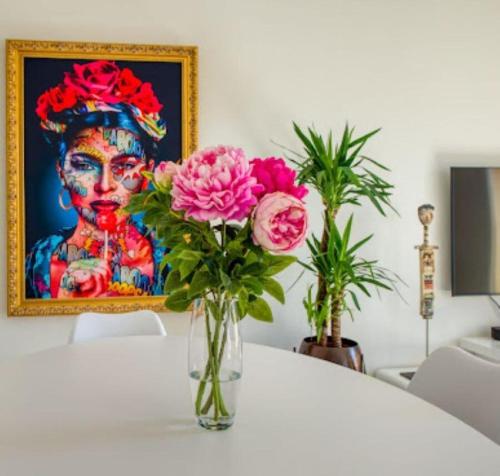 un vase avec des fleurs roses sur une table avec une peinture dans l'établissement Grand deux pièces - Hyper Centre, à Nice