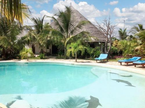 a swimming pool in front of a house with palm trees at 3 bedrooms house at Watamu 100 m away from the beach with shared pool furnished terrace and wifi in Watamu