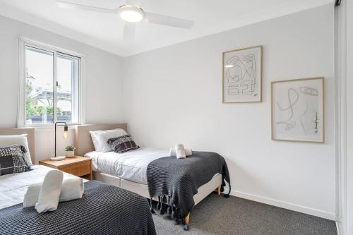 a white bedroom with two beds and a window at Beautiful Balmain Abode - Balmain, NSW in Sydney