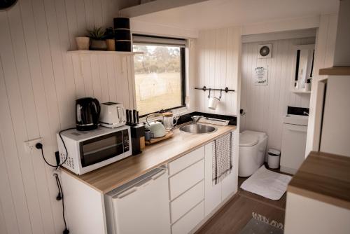 a small kitchen with a microwave and a sink at Odyssean Tiny House B in Cessnock