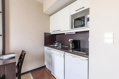 a small kitchen with white cabinets and a table at Appart’City Confort Nantes Ouest Saint-Herblain in Saint-Herblain